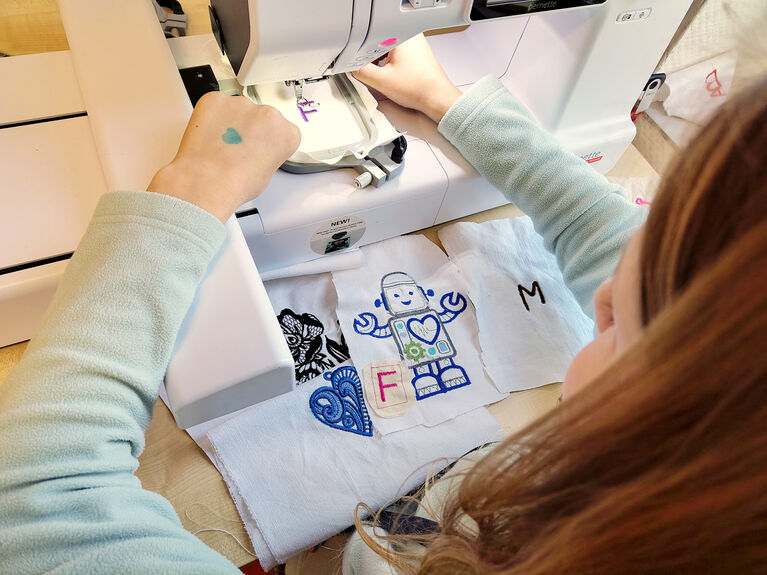 Eine Person näht mit einer Stickmaschine ein Robotermotiv auf weißen Stoff.