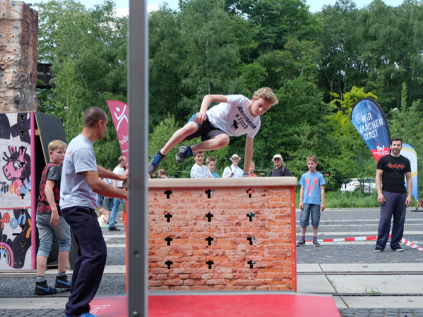 Ein männlich gelesenes Kind springt über eine kleine Mauer.