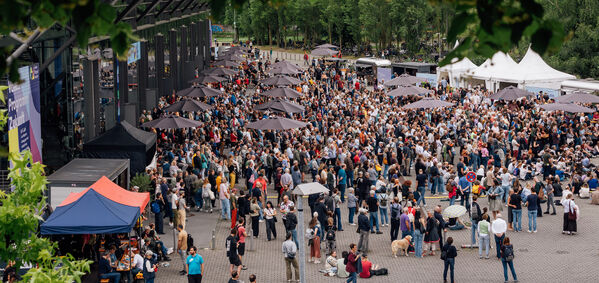 Besucher*innen einer Veranstaltung auf einem gepflasterten Platz mit vielen Pavillons