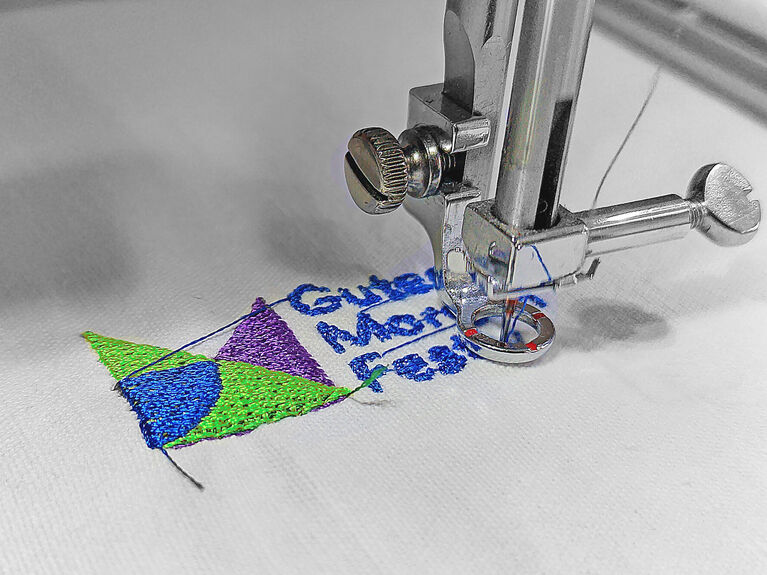 Nahaufnahme einer Nähmaschine, die bunte Formen und Text auf Stoff stickt.