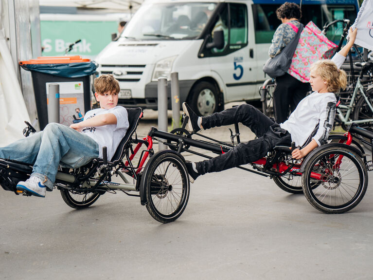 Zwei Jungen sitzen im Freien auf Liegedreirädern in entgegengesetzte Richtungen.