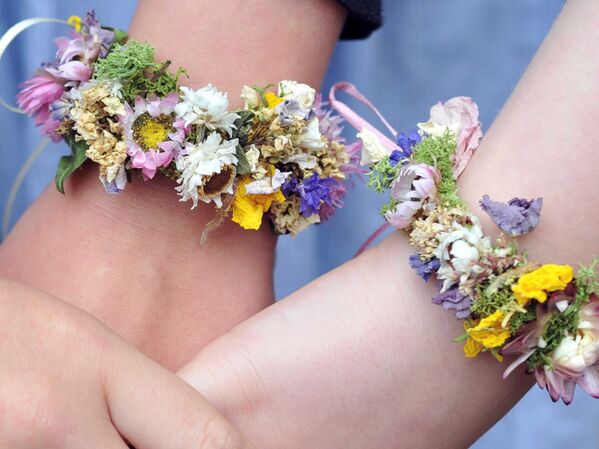 Drei Arme mit bunten Blumenarmbändern, die Hände ineinander verschränkt.